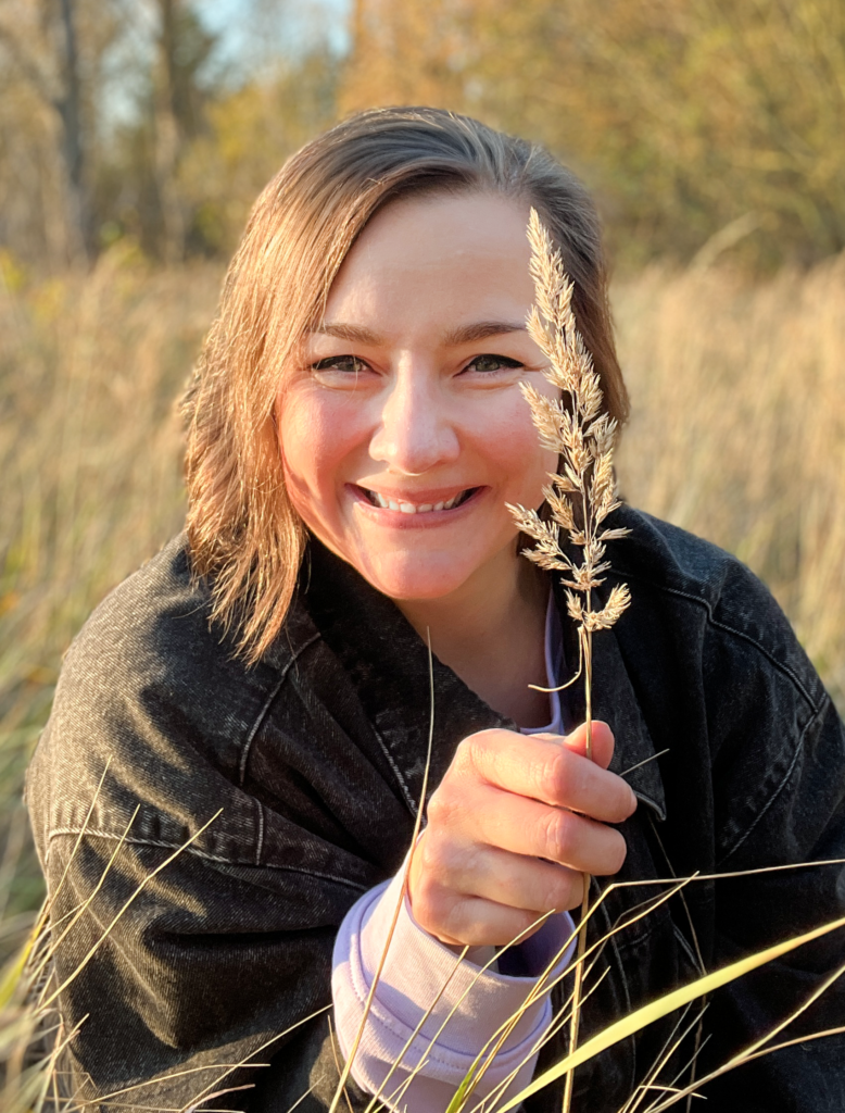 Constanze Bechtold lächelt in die Kamera und hält eine Grasrispe im goldenen Herbstlicht – authentisches Portrait der Coachin und Reiki Meisterin