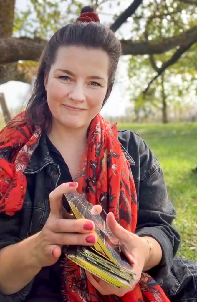Constanze Bechtold sitzt unter einem Baum und hält Tarotkarten in den Händen – Tarot als Teil der 1:1 Begleitung im Coaching-Programm Lebendig