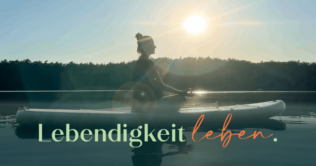 Constanze Bechtold meditiert im Schneidersitz auf einem SUP-Board bei Sonnenuntergang auf einem stillen See.